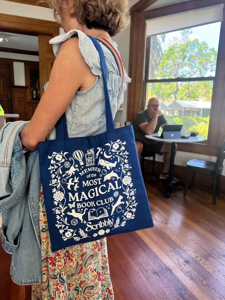 The navy Most Magical Book Club tote bag worn over a shoulder